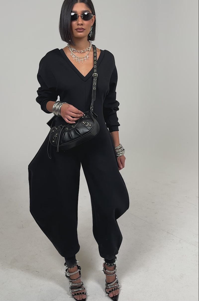 Video of woman modeling COMFY COZY SWEATSHIRT JUMPSUIT IN BLACK, paired with dark sunglasses and strappy heeled sandals