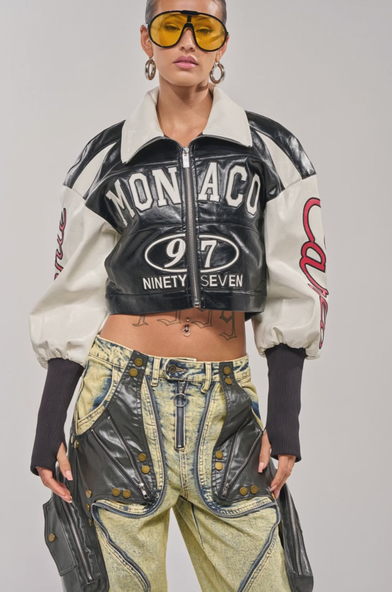 Video of woman modeling the LET'S RACE EMBROIDERED BOMBER—a cropped, black and white faux leather jacket—paired with light-wash high-waisted pants with bold black accents and visible tattoos.