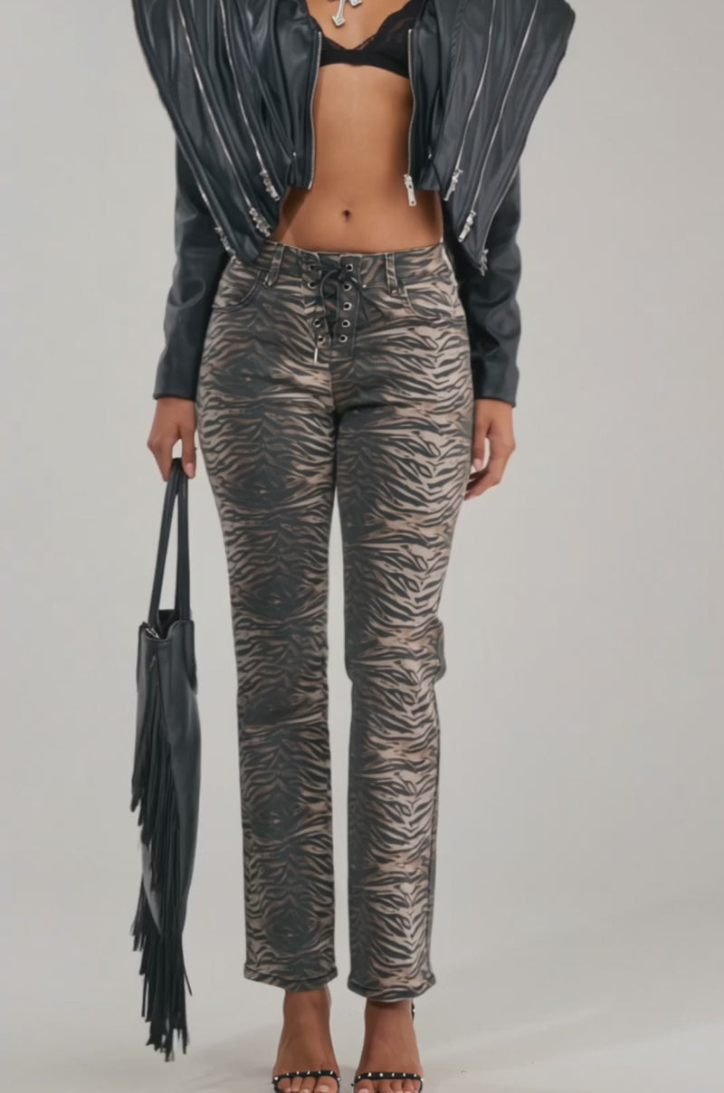 A video of a woman in large sunglasses, the COSMO ZIPPER MOTO faux leather jacket with an oversized collar, a black bralette, metallic animal-print pants, and heels. 
