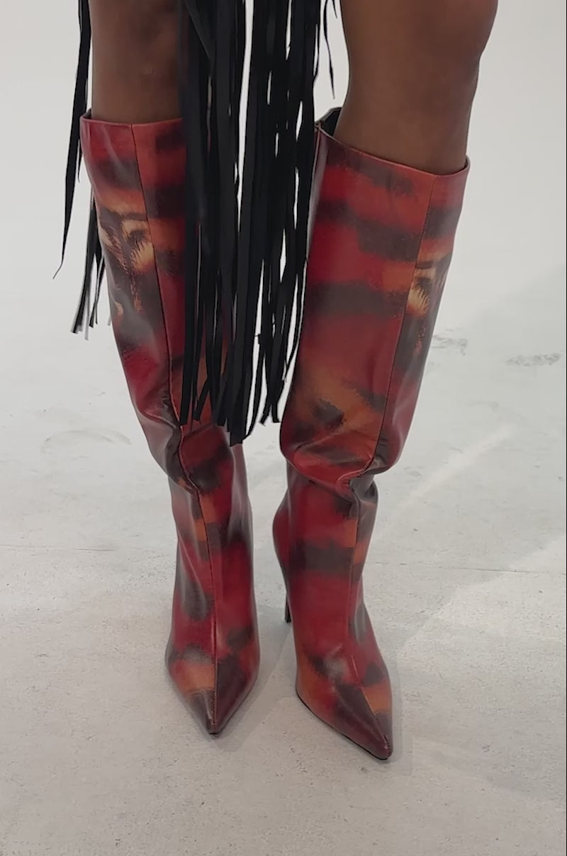 A video of a model wearing the AKIRA GOLD CAELIX TIGER PRINTED STILETTO BOOT—featuring a striking orange tiger print with a bold tiger face design and red accents.