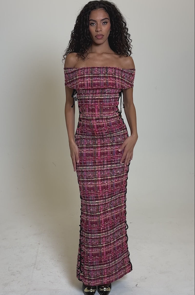 Video of woman modeling the JUST A GIRL TWEED MAXI DRESS, an off-the-shoulder maxi with pink, black, and yellow tweed hues, lace-up side paneling, curly hair, neutral makeup, and black heels for a modern look.