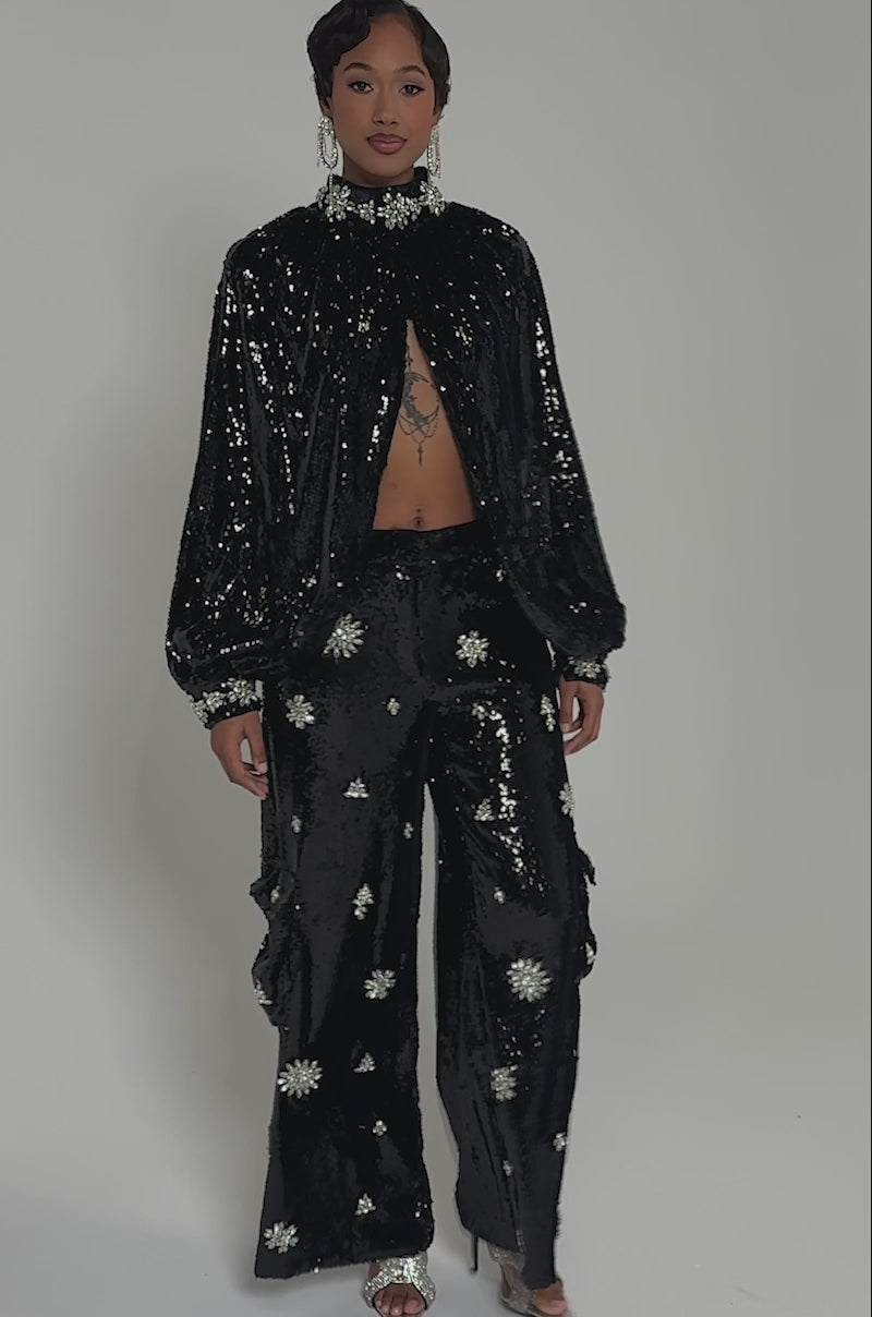 Video of woman modeling the DAZZLING HOLIDAY SEQUIN WIDE LEG CARGO PANT with a matching loose-fit cropped top featuring silver starbursts, paired with statement earrings and silver sandals for a festive holiday look.