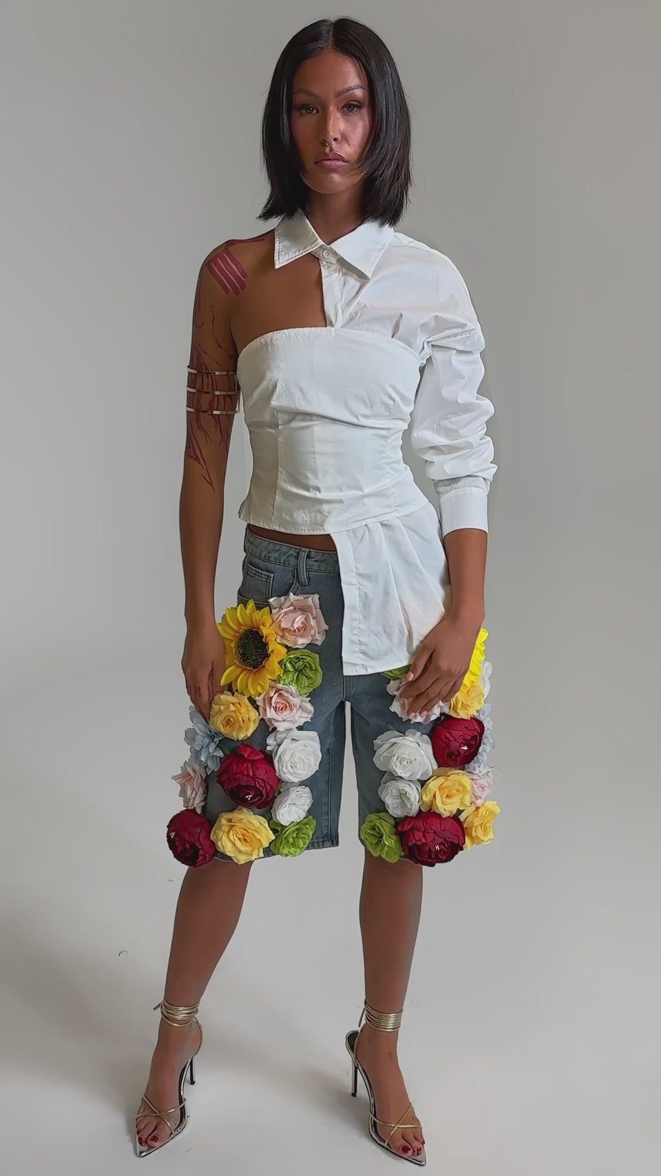 A video of a woman in the FLOWER POWER BERMUDA SHORT, featuring high-rise denim and vibrant floral appliques. 