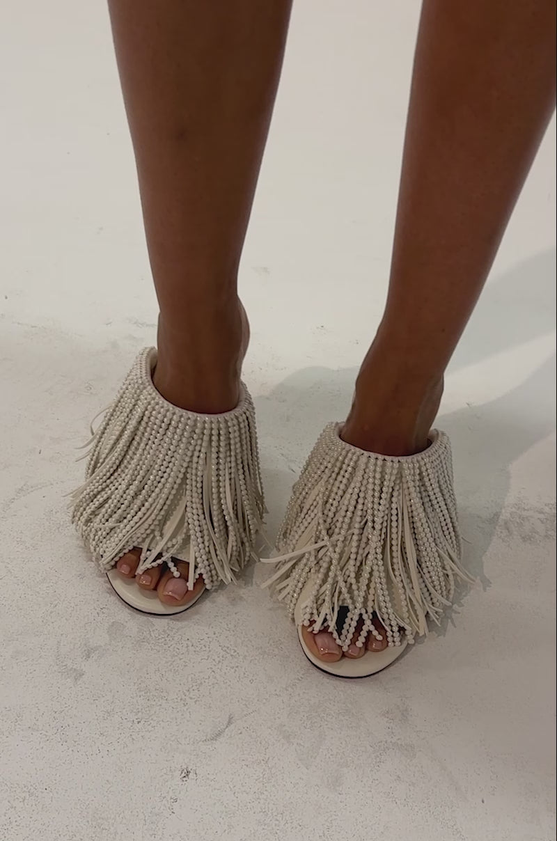 Video of a woman modeling the AZALEA WANG BRIELLE BONE PEARL FRINGE WEDGE SANDAL—an ivory faux leather wedge sandal adorned with long, beaded fringe.