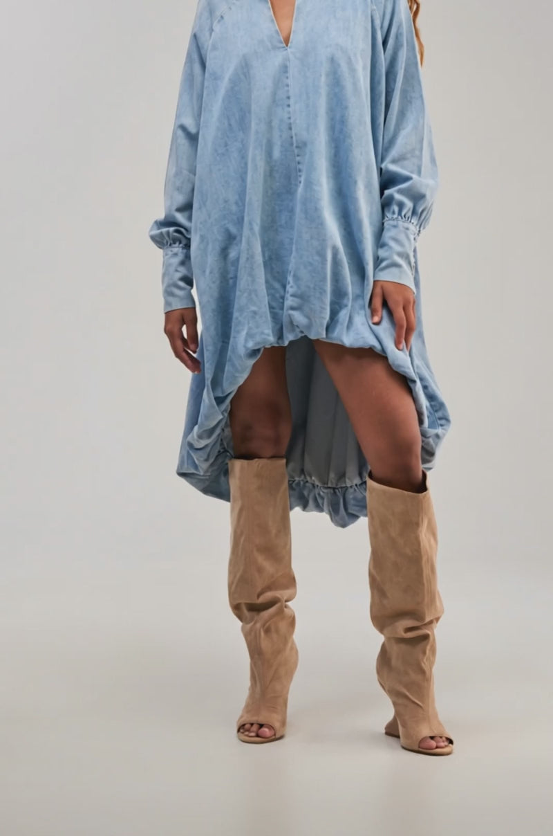Video of a woman modeling the AMELIA DENIM HIGH-LOW DRESS in light blue, styled with beige knee-high slouchy boots.