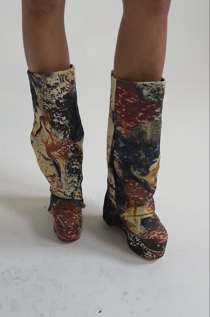 A video of a person wearing the AZALEA WANG FRANKEYE MULTI MATERIAL FLATFORM BOOT with knee-high platform design and a multicolored splatter paint denim pattern in blue, red, yellow, and cream against a plain background.