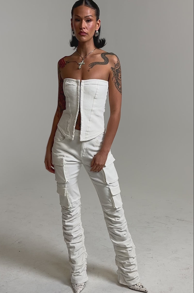 A video of a woman in the IT GETS EASIER STACKED CARGO PANT IN WHITE, pairing the ruched, pocketed skinny-leg style with a strapless top, pointed-toe shoes, and a necklace. 