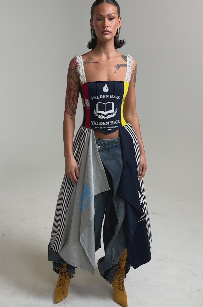 A video of a woman in festival attire, pairing the UNIVERSAL CORSET with wide-leg jeans, yellow boots, and a flowing skirt made from layered "Yalden Hall" T-shirts, set against a plain light background.