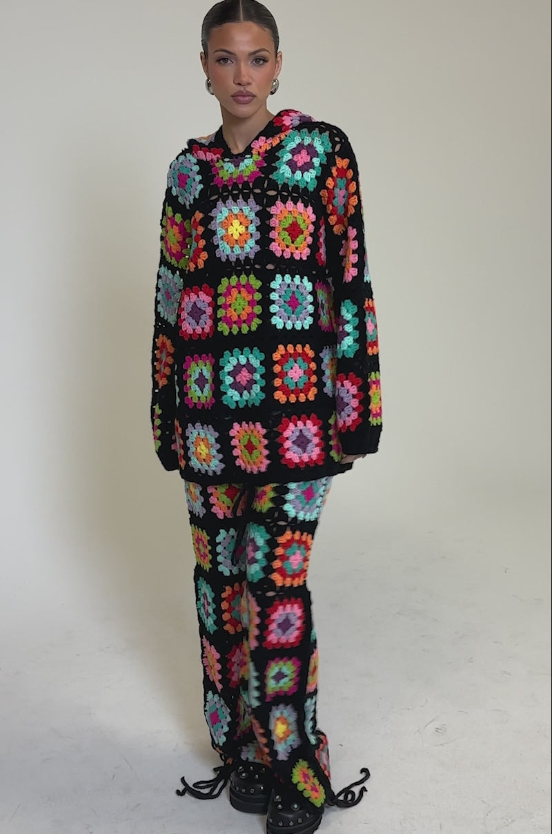 Video of woman modeling the FESTIVAL GIRLY OVERSIZED CROCHET SWEATSHIRT IN MULTI, a colorful granny-square patchwork set with black borders, paired with loose pants and chunky black shoes for a vibrant, standout look.