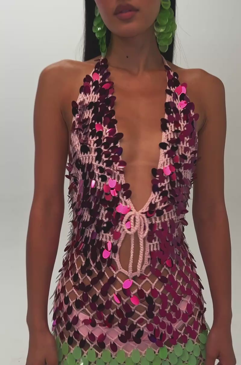 Video of a woman modeling the PARTY CRASHER SEQUIN MAXI DRESS IN GREEN MULTI—a long, form-fitting crochet halter maxi adorned with large, vibrant sequins in pink, green, silver, and holographic hues—she stuns with a deep plunging neckline.