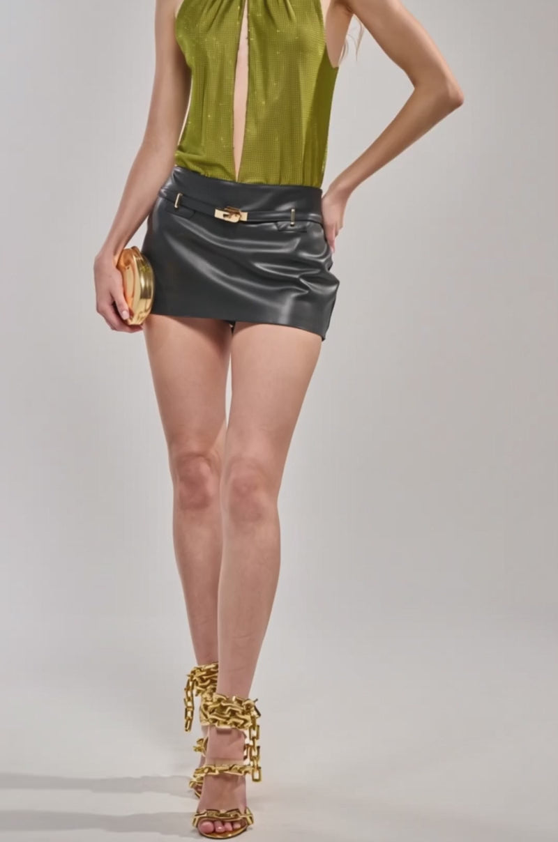 Video of woman modeling the SHINING DOWN ON YOU RHINESTONE BODYSUIT IN GREEN, styled with a black leather skirt and holding a small round clutch against a plain light background.