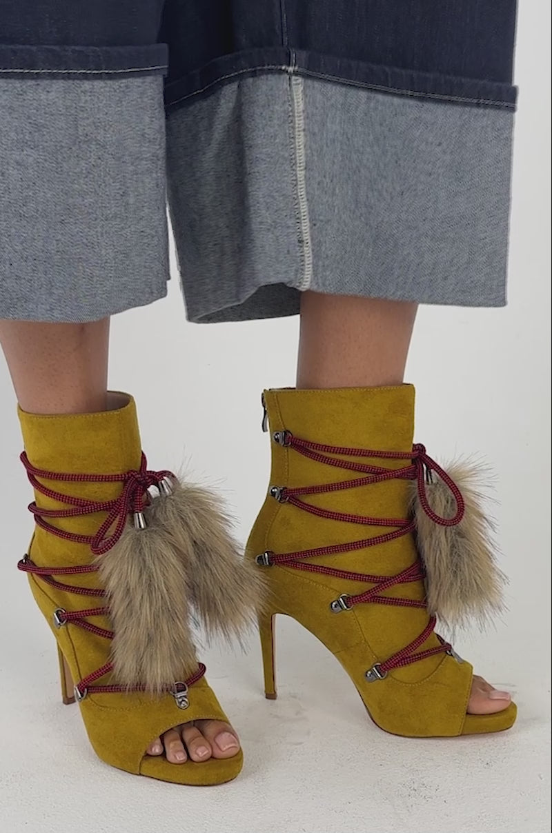 Video of a woman modeling the AZALEA WANG MIRA MUSTARD OPEN TOE FAUX SUEDE BOOTIES featuring stiletto heels and faux fur tassel accents.