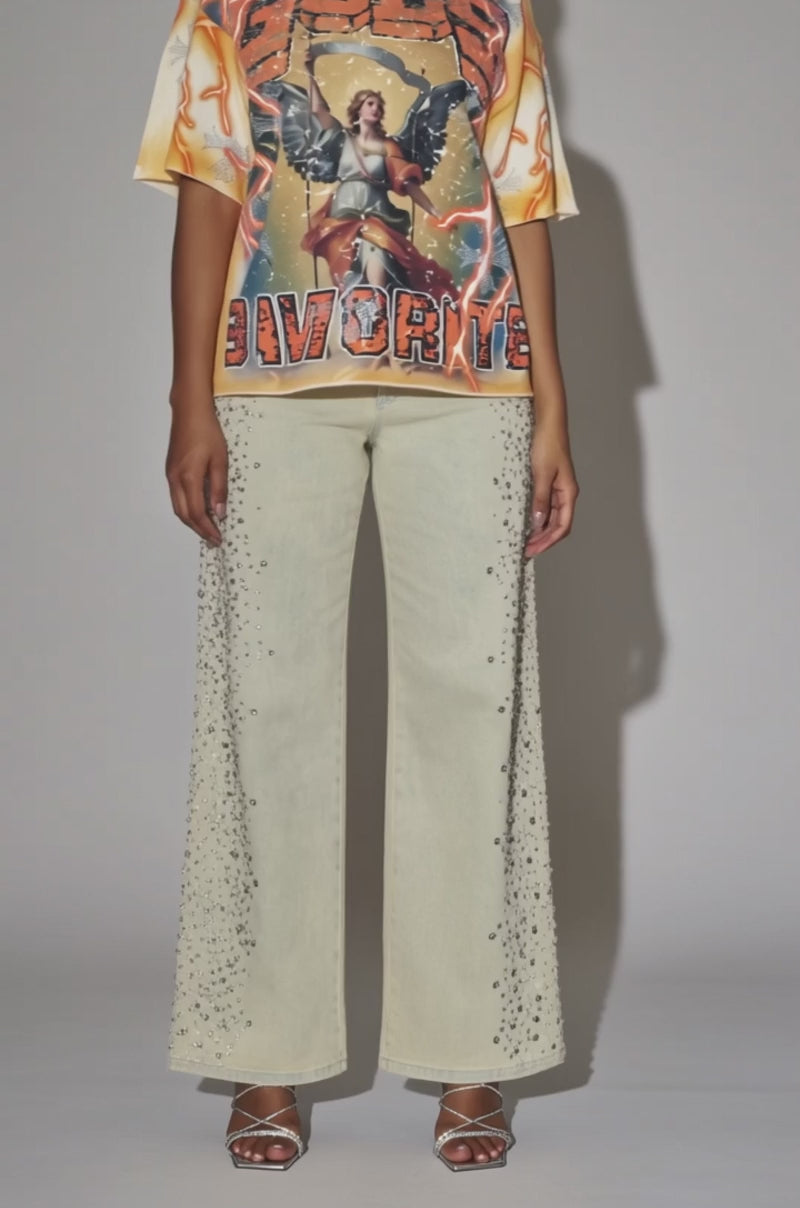 A video of a woman in a GOD'S FAVORITE CANVAS T-SHIRT paired with embellished light wide-leg pants and silver high-heeled sandals.