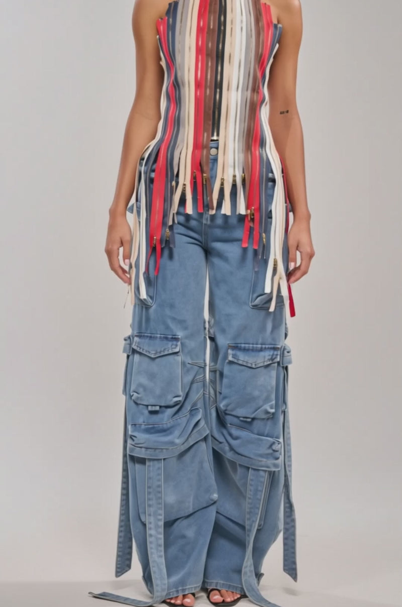 Video of woman modeling the ZIPPED UP HALTER TOP, a corset-style piece with red, beige, white, and brown vertical strips and zipper pulls, paired with blue cargo jeans—making for standout festival wear against a plain light background.