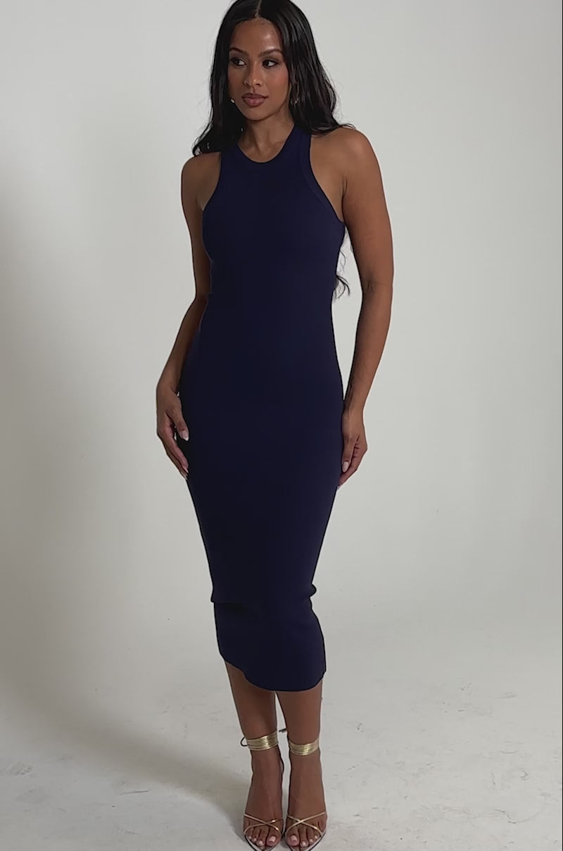 Video of woman modeling the CUTIE PIE KNIT MIDI DRESS IN NAVY—a sleeveless, body-skimming midi dress—paired with gold high-heeled sandals against a plain light gray background.