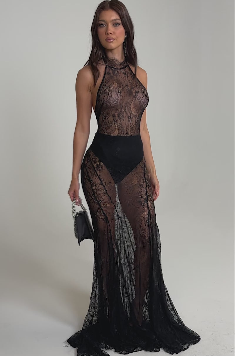 Video of woman modeling the NEVER BETTER MOCK NECK LACE MAXI DRESS IN BLACK, featuring a high neckline and flowing train. She holds a small black handbag, her long wavy hair down against a plain light background.