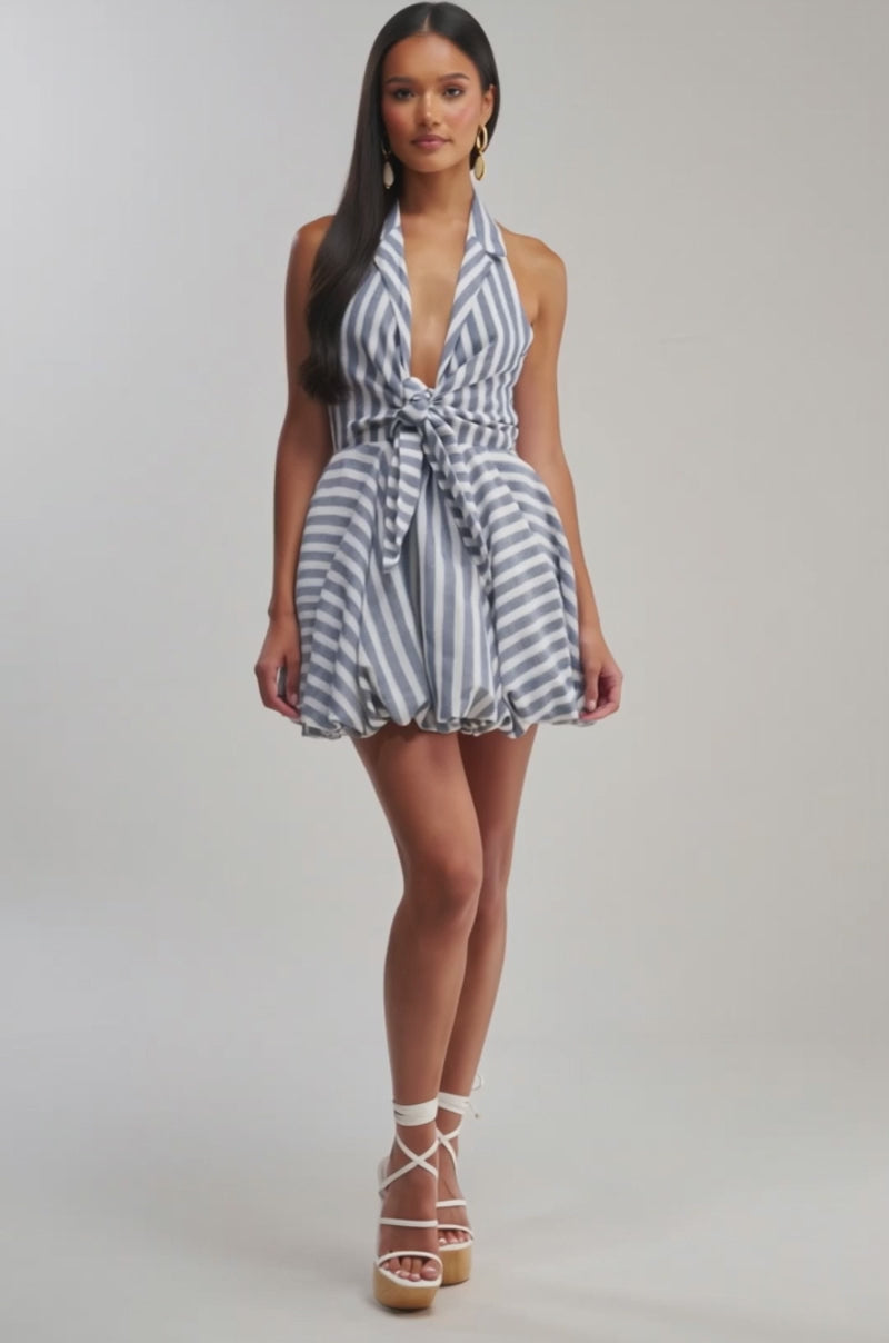 Video of woman modeling the BRUNCH PLANS STRIPED MINI DRESS IN BLUE, featuring nautical stripes, a sleeveless halter neckline, front knot detail, and a flared balloon-style skirt against a plain background.
