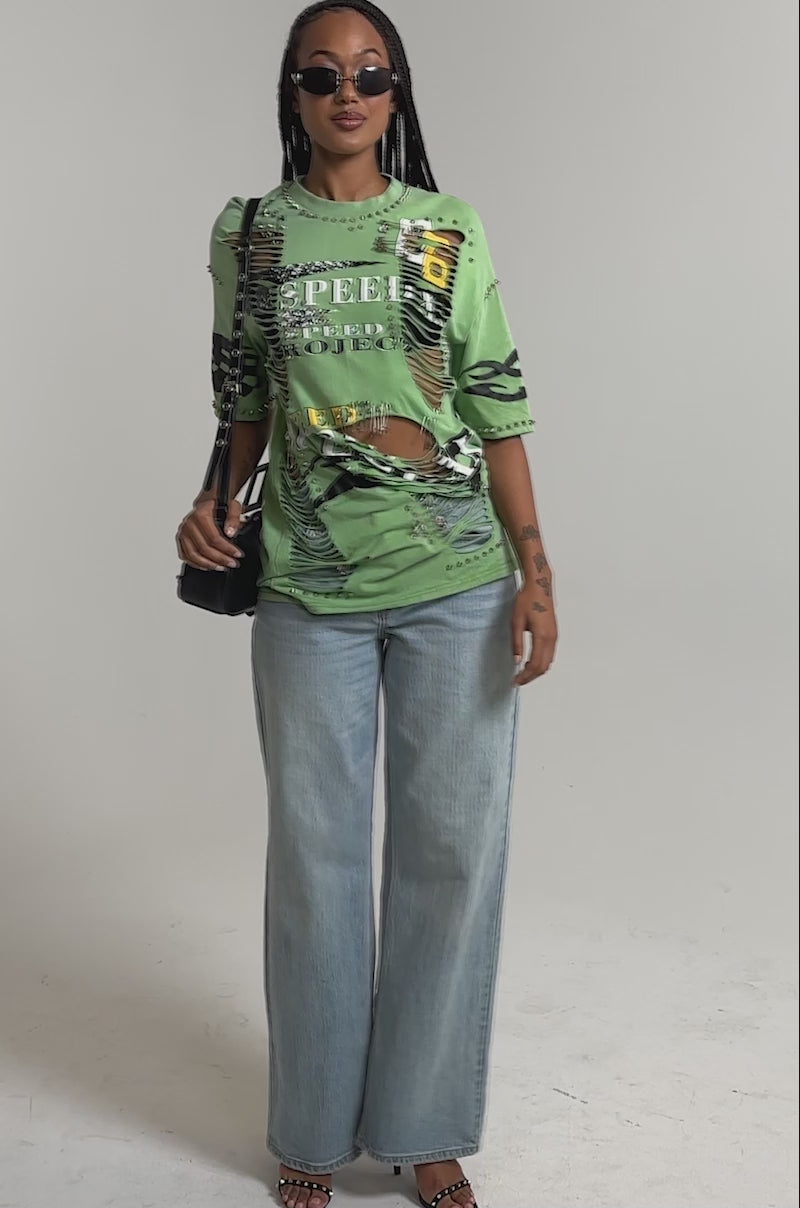 A video of a woman wearing the NEVER TOO MUCH DISTRESSED OVERSIZED TEE, styled with sunglasses, light blue wide-leg jeans, black heeled sandals, and a black shoulder bag.