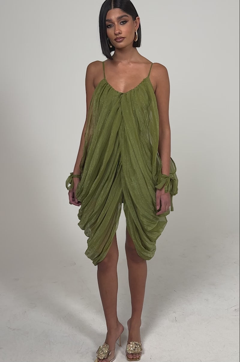 A video of a woman wearing the VIVA LA VIDA MESH DRESS, an olive midi dress with thin straps, a high-low hemline, and a light, airy mesh design. 