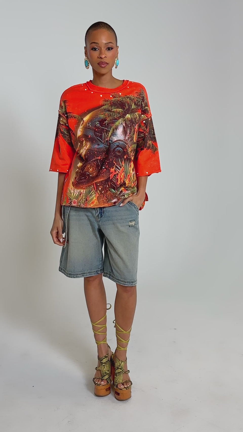 Video of woman modeling the FIRST ROW LOST PARADISE RHINESTONE FRENCH TERRY TEE—an oversized orange graphic tee with a tropical scene—paired with light blue jean shorts.