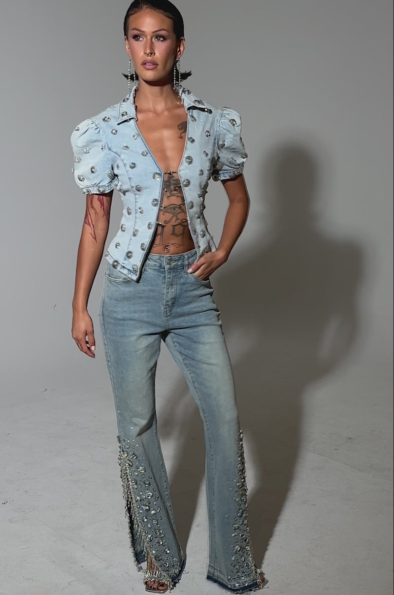 A video of a woman wearing the STAR GIRL RHINESTONE DENIM set: a light blue jacket with puffed sleeves, pearl and rhinestone accents, and matching high-rise jeans featuring pearls and side slits.