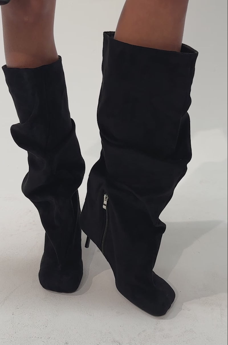 Video of a woman modeling the AZALEA WANG RANDALL Black Suede Slouchy Stiletto Boots with heels, paired with a small black handbag featuring silver accents.