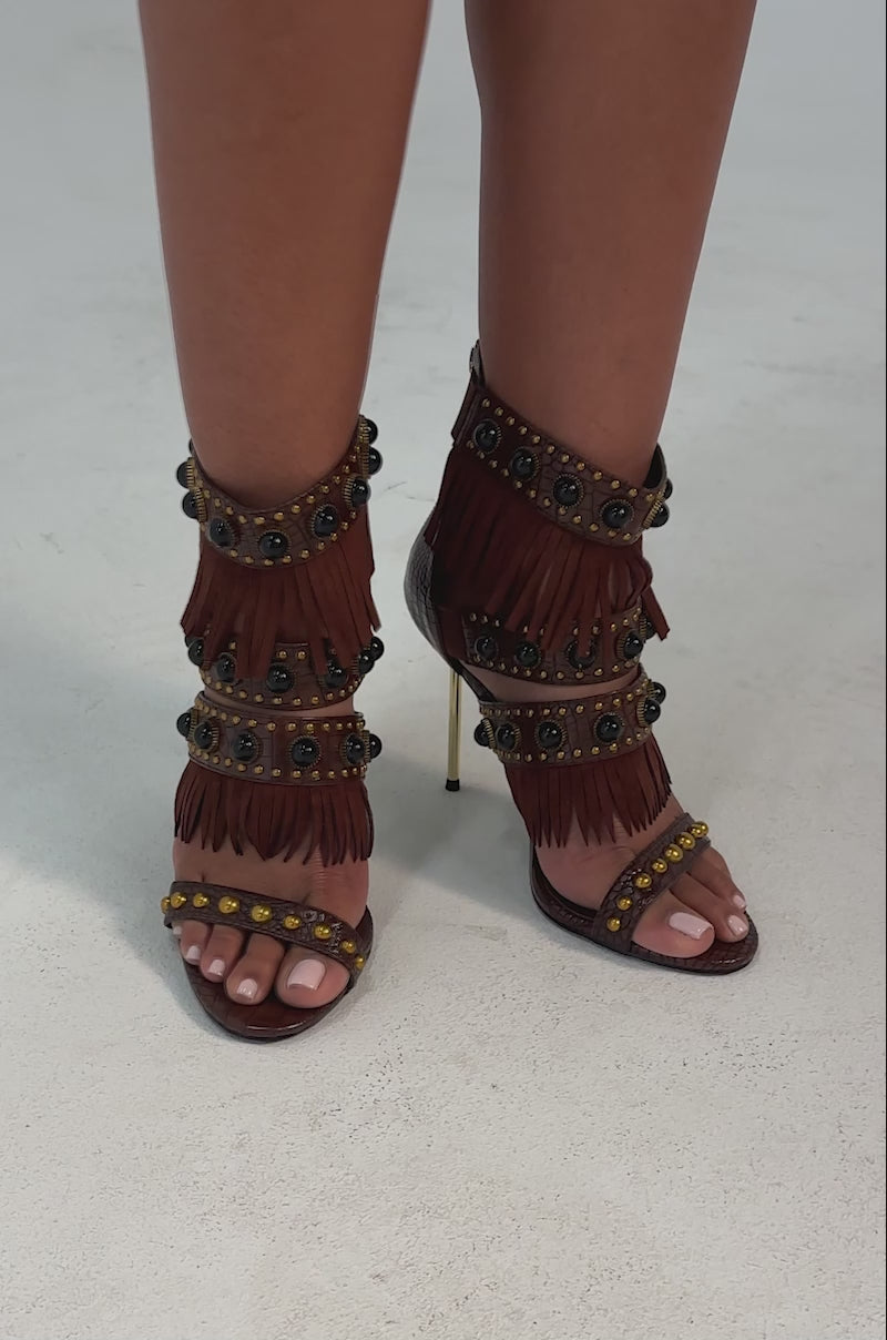 A video of a person wearing the AZALEA WANG ANTOINE brown fringe and gold embellished stiletto heel, featuring croc-embossed faux leather.