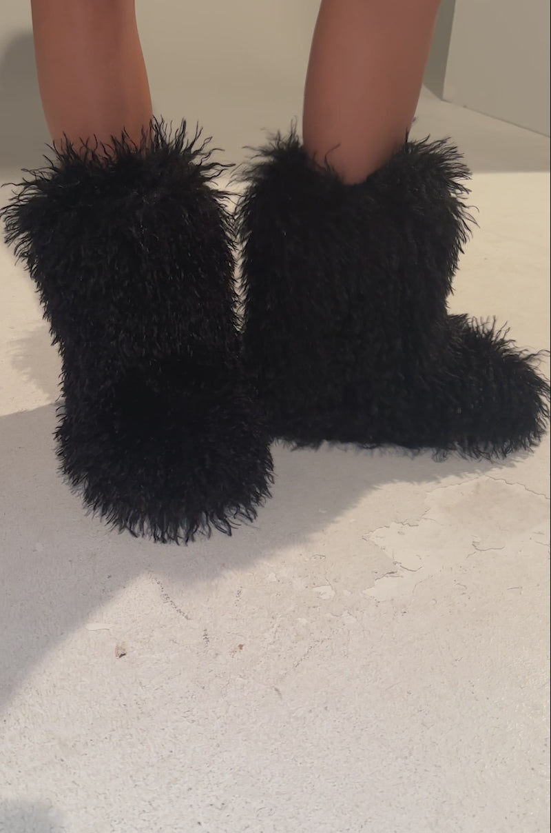 A video of a person wearing AZALEA WANG AZAD BLACK MOHAIR FLAT BOOTIE boots standing against a gray background, revealing a tattooed thigh.