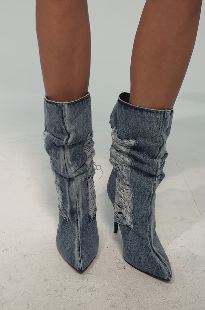 A video of a model wearing the AZALEA WANG NAELIA DENIM STILETTO BOOTIE. The bootie is a bold, high-heeled pointed-toe bootie in blue denim with a slouchy shaft and frayed distressed patch.