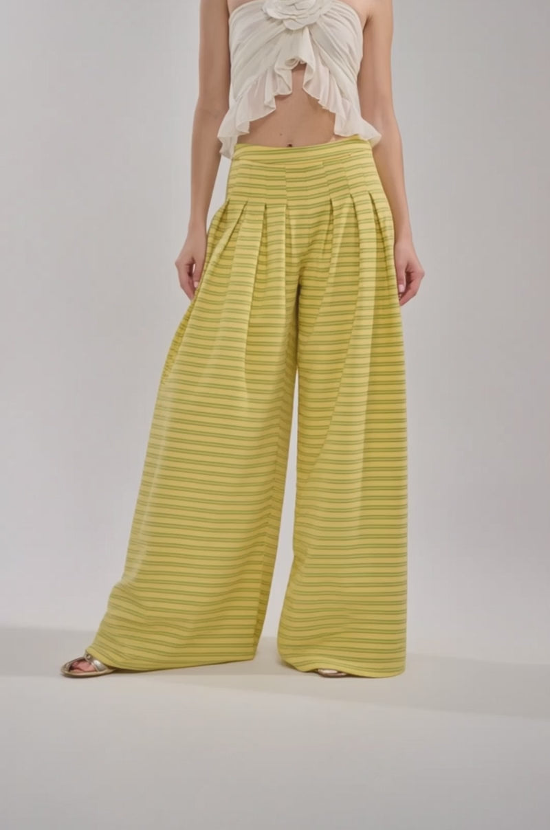 Video of woman modeling the SILVER COAST YELLOW STRIPE TROUSER, which are high-waisted, wide-leg summer trousers with horizontal yellow stripes and pleats, paired with a ruffled white crop top against a plain, light background.