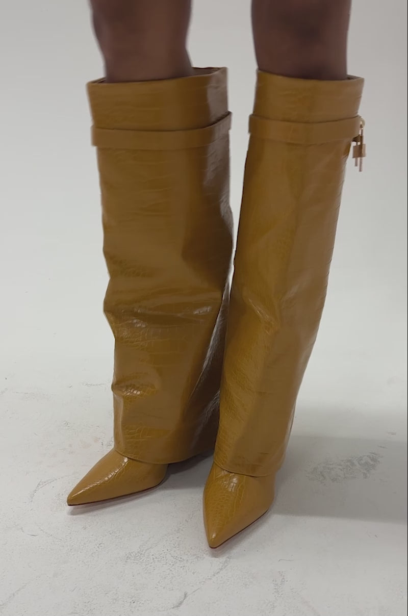 Video of a woman modeling the AZALEA WANG ENZO MUSTARD CROC SHARK BOOT—these shiny, textured mustard knee-high foldover boots feature pointed toes and low heels.
