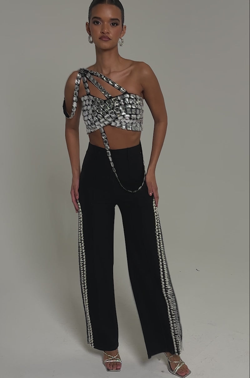 Video of woman modeling the FLASHING LIGHTS BLOUSE—a shiny one-shoulder crop top with large square embellishments—paired with black high-waisted pants.