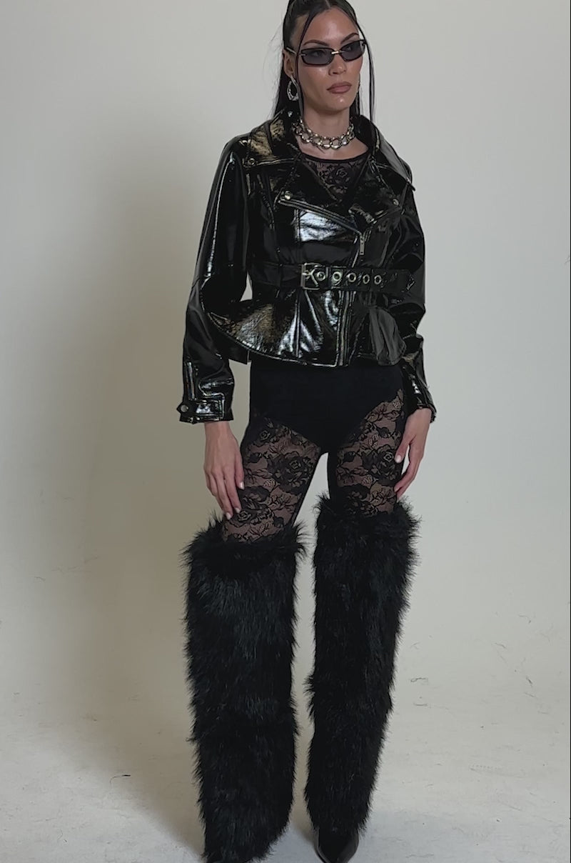 Video of woman modeling the PEP IN MY STEP PATENT MOTO jacket over a sheer black lace bodysuit, styled with sunglasses, hoop earrings, and a chunky chain necklace against a neutral background.