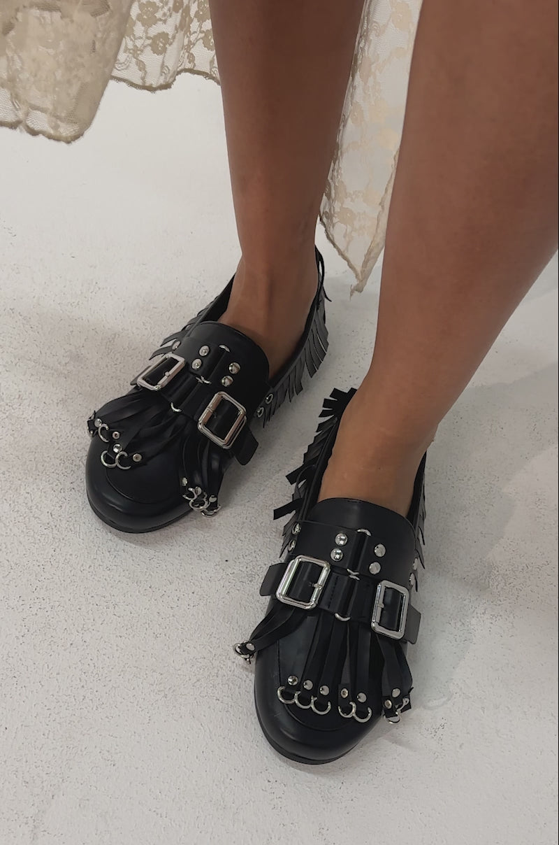 Video of woman modeling the AZALEA WANG SEVYN Black with Silver Hardware Flat Loafers featuring almond toes, silver buckles, studs, fringe, and eyelet accents.