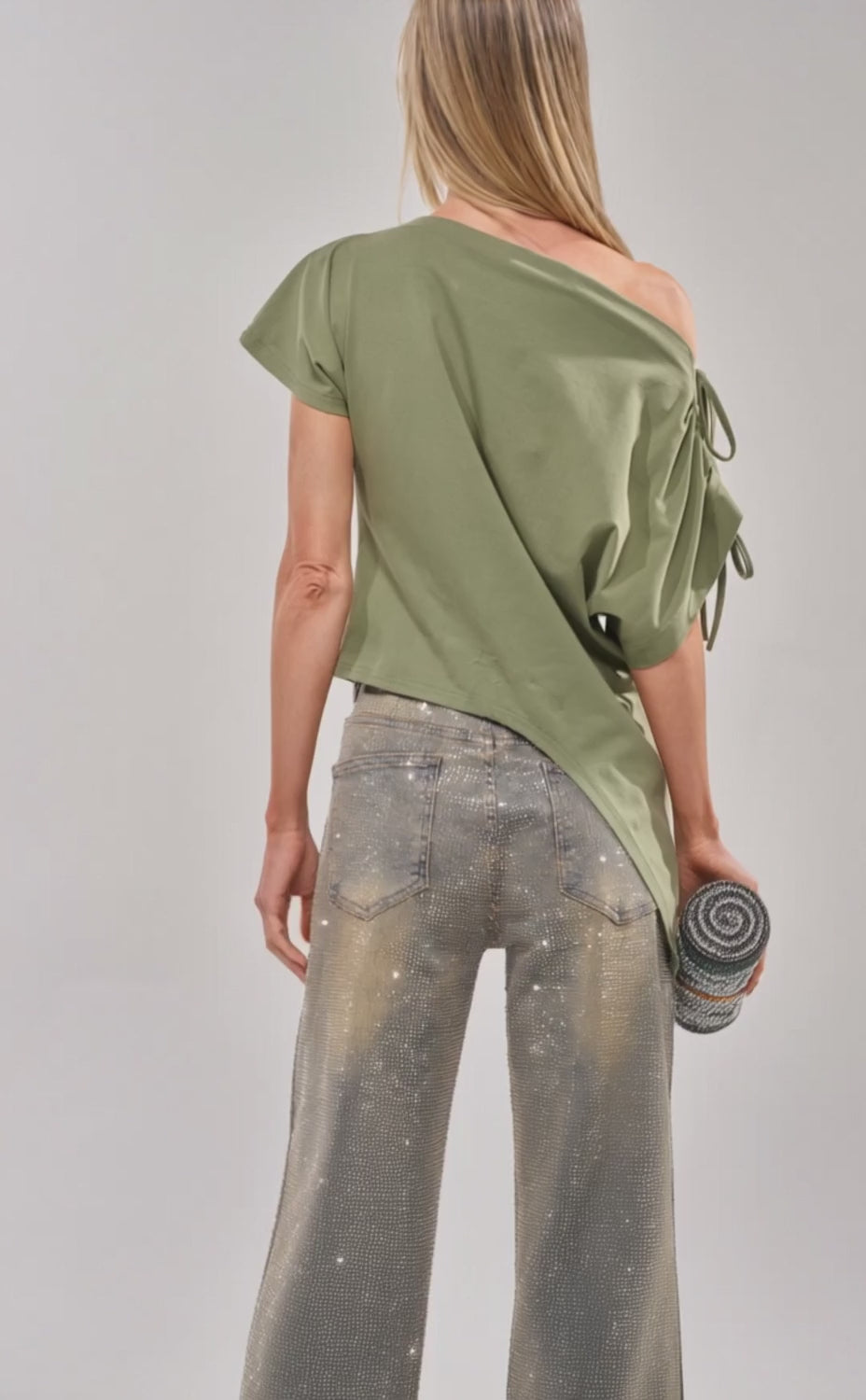 Video of woman modeling the THE RUMORS ARE TRUE OFF THE SHOULDER OLIVE TEE and light blue rhinestone jeans, standing against a plain background.