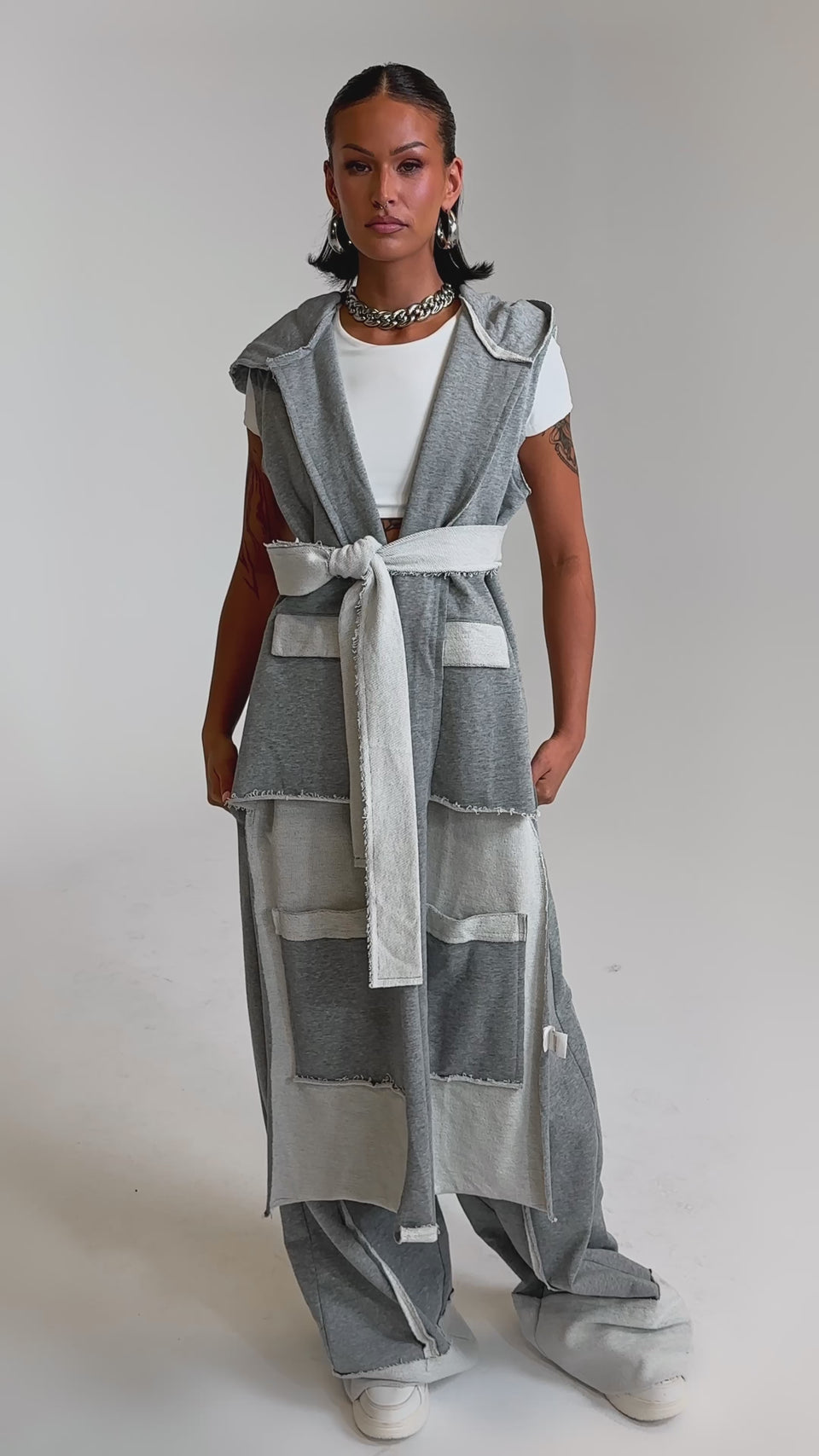 A video of a woman in thesleeveless, hooded gray vest, IM UP NEXT TROUSER high-rise cotton pants with patch pockets, a white crop top, chunky sneakers, and jewelry. 