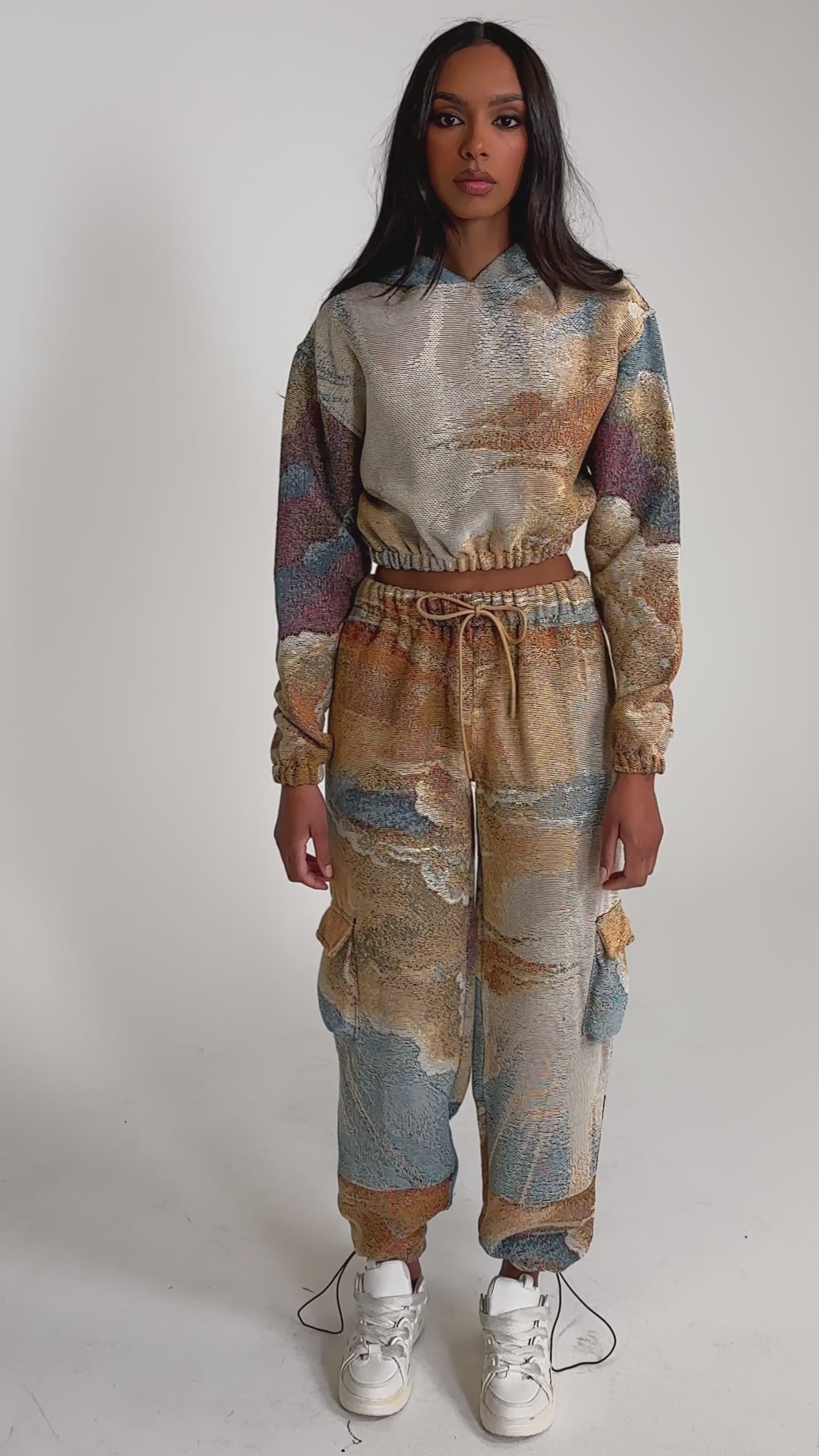 Video of woman modeling the INTO THE WILD WIDE LEG JOGGER and a matching hoodie with a colorful abstract print, paired with white sneakers against a plain light background.