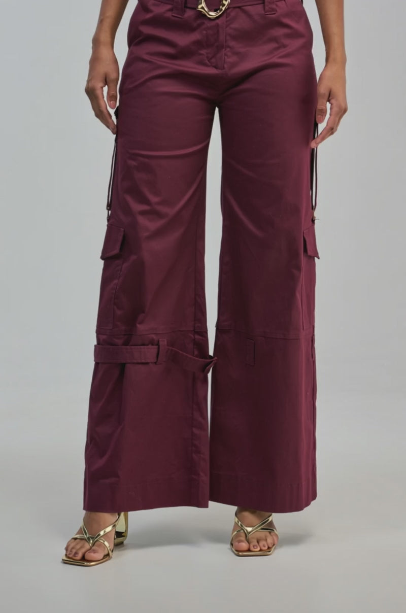 Video of a woman modeling the FLORENCE PLUM TROUSER, featuring a high-waisted, wide-leg silhouette and side pockets in a rich maroon hue.