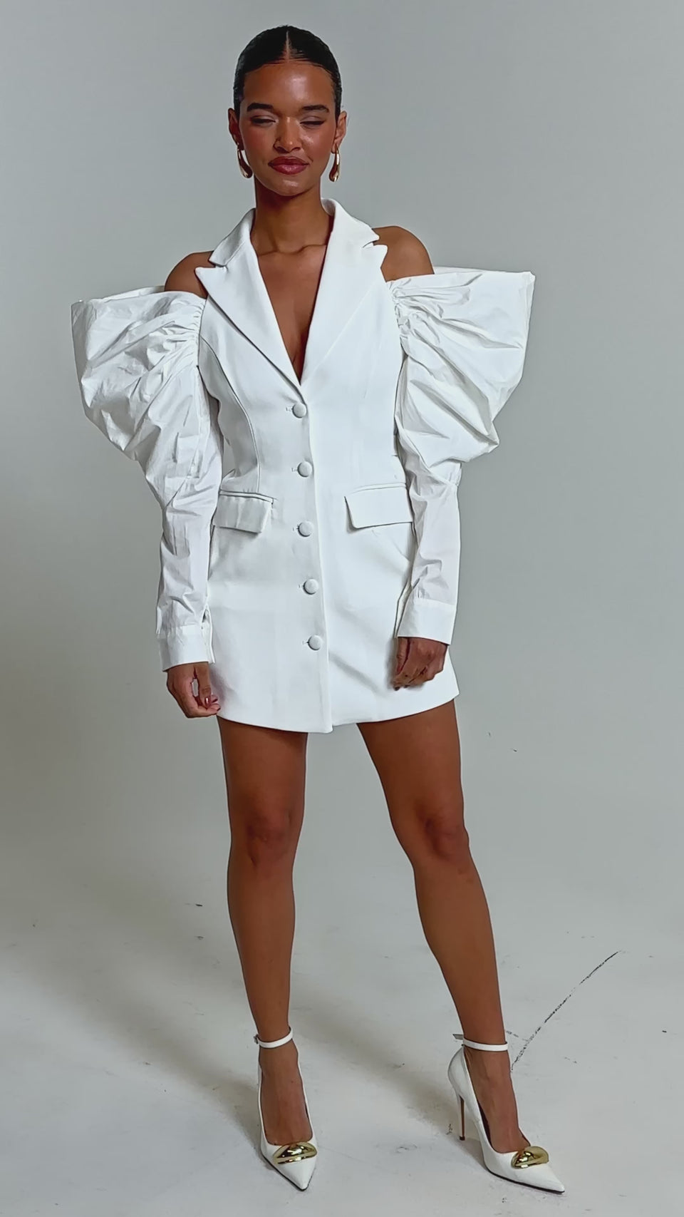 Video of woman modeling the RUNNING THINGS COLLARED MINI DRESS, a white mini dress featuring structured off-the-shoulder puffed sleeves and button details, set against a plain light background.