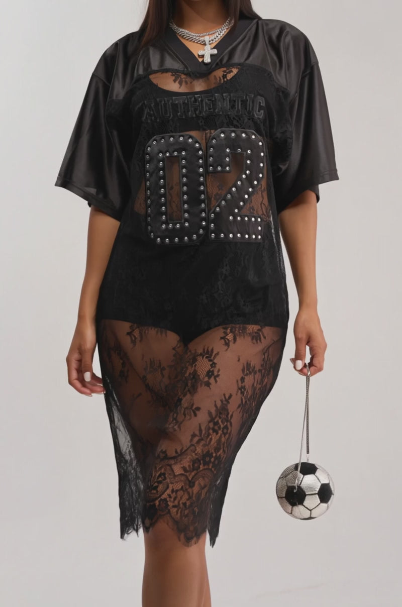 A video of a woman in the PART TIME PLAYER LACE JERSEY MIDI DRESS IN BLACK with "02" and "AUTHENTIC" lettering, paired with a black beanie, layered necklaces, and a soccer ball purse.