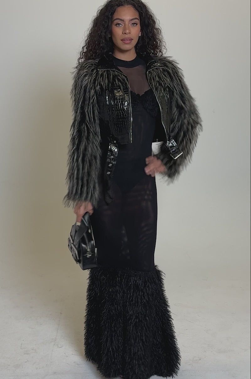 Video of woman modeling the LIGHT IT UP FUR TRIM MOTO, a black moto jacket with a high collar and belt, over a sheer black outfit against a plain light background.
