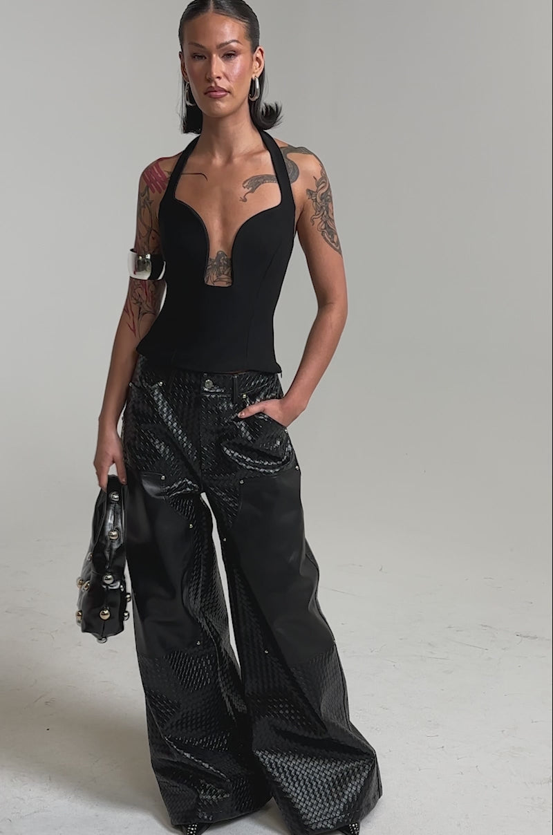 A video of a woman wearing the TRY ME HALTER TOP IN BLACK and shiny, wide-leg black pants. 