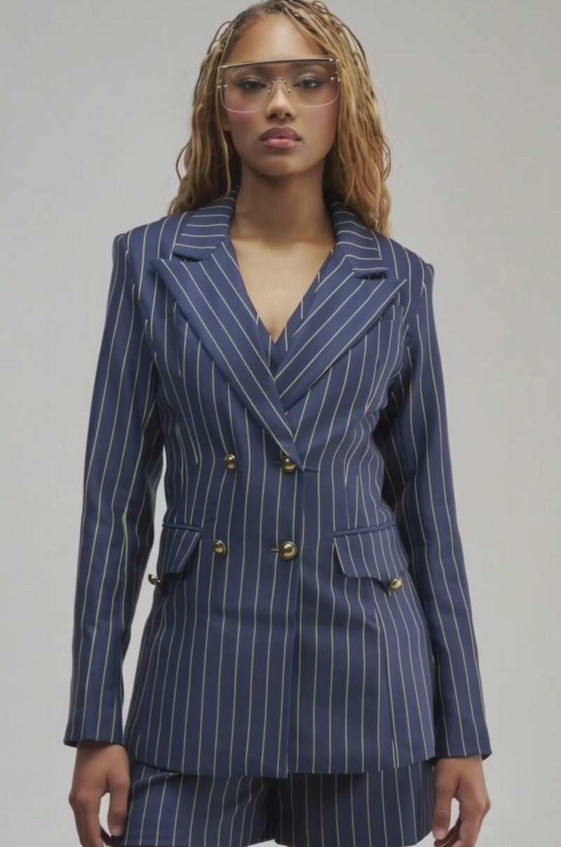 Video of a woman modeling the SUNDAY PINSTRIPE BLAZER—a navy blue double-breasted pinstripe blazer with gold buttons—paired with matching shorts. 