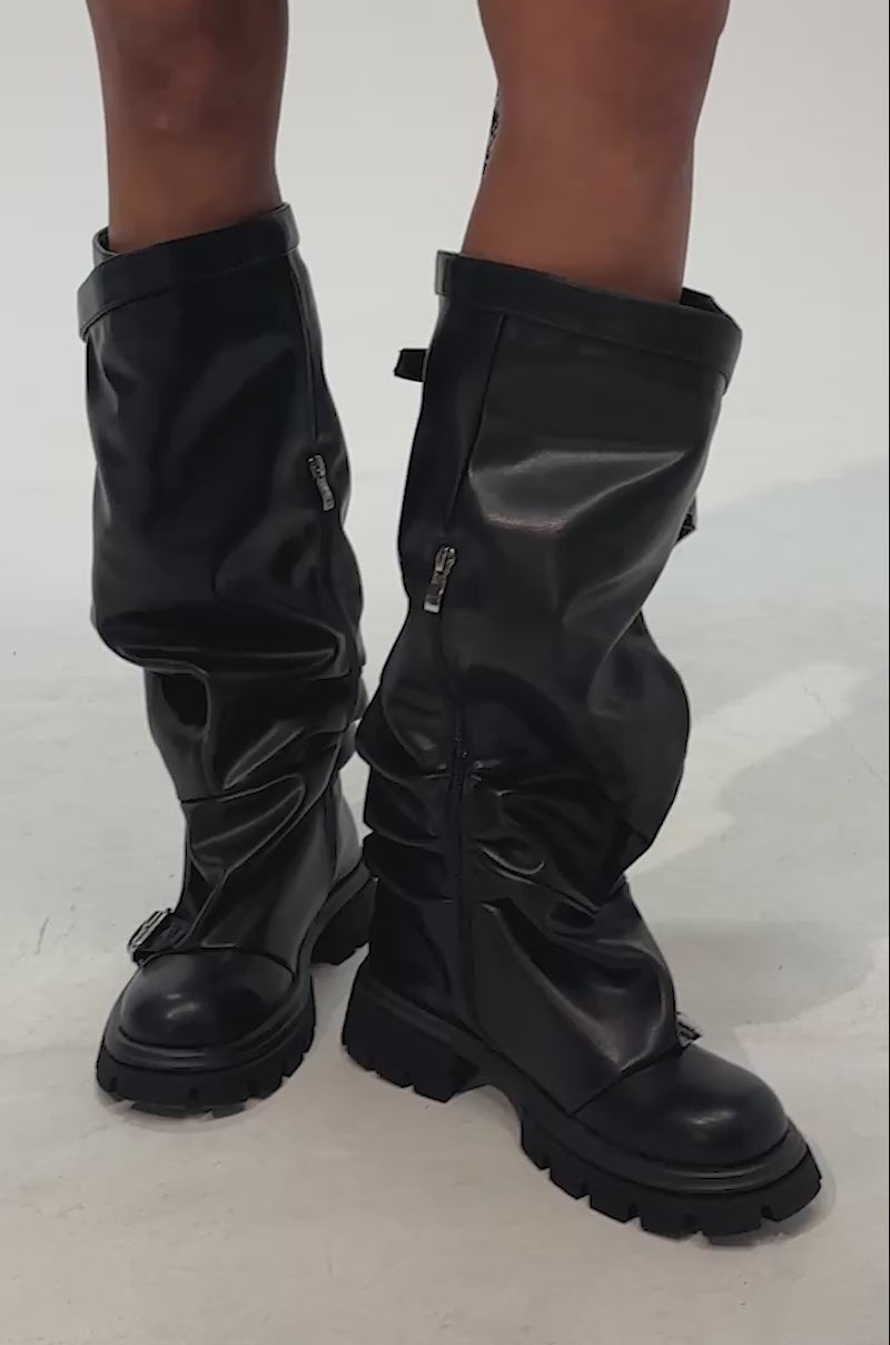 Video of woman modeling the AZALEA WANG GOMEZ BLACK KNEE HIGH BOOT—knee-high, black leather boots featuring chunky soles and side zippers reminiscent of classic combat boots.