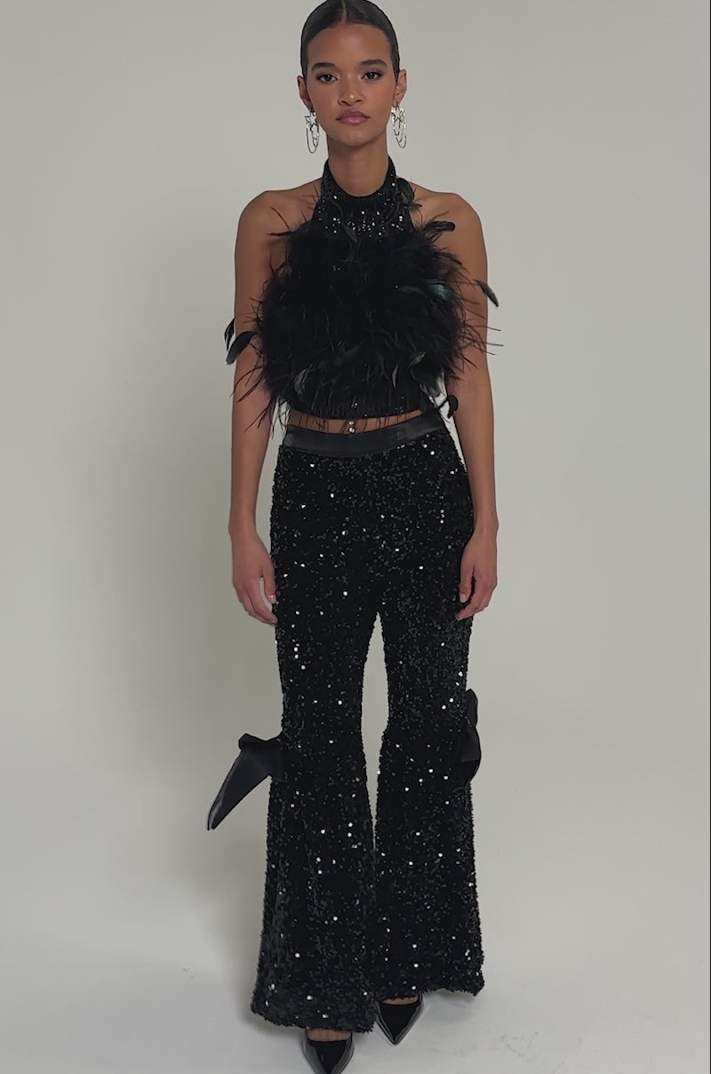 Video of woman modeling the SELENA SPARKLING WIDE LEG PANT featuring large black bows on the knees, styled with black pointed-toe heels and a cropped top. Her hands rest at her sides against a plain, light-colored background.