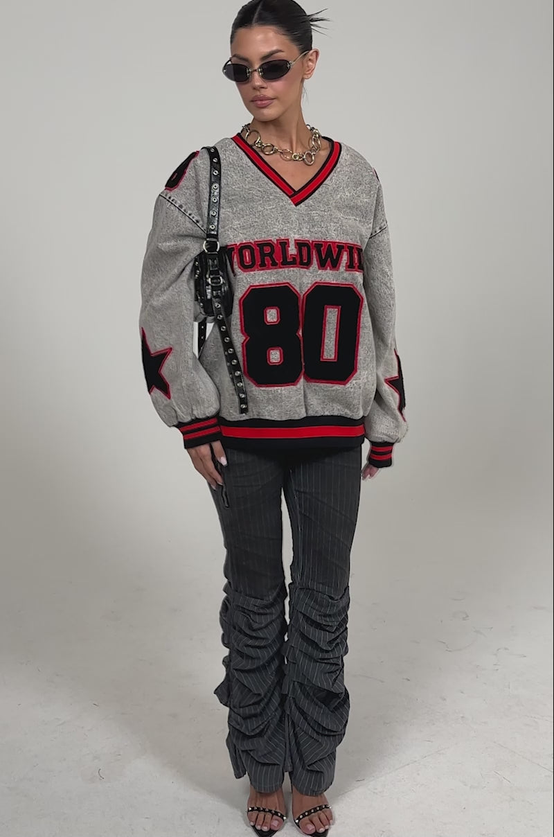 Video of woman modeling the TALK TO ME STRIPE TROUSER, a cropped jacket with red and black star sleeve details, a studded black handbag, and open-toe heeled sandals.