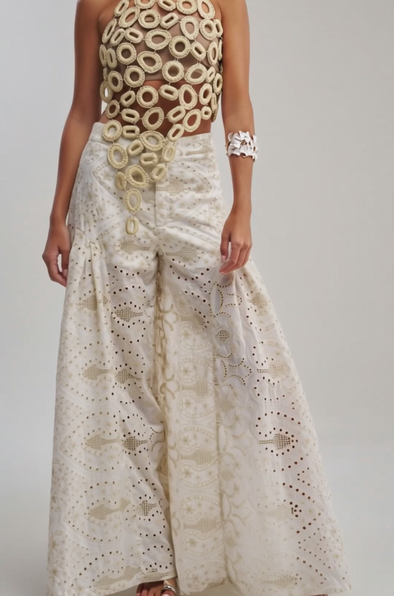 Video of woman modeling the BEACH VIBES CHAIN TOP, featuring large crocheted loops, paired with white patterned pants and a chunky coral-shaped bracelet. She stands against a plain light background.