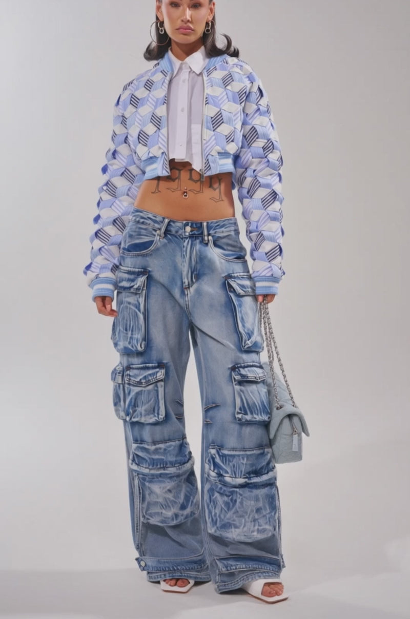 Video of woman modeling the BOP AND WEAVE POPLIN BOMBER over a white cropped shirt and loose blue jeans, accessorized with large hoop earrings and showing tattoos on her torso.