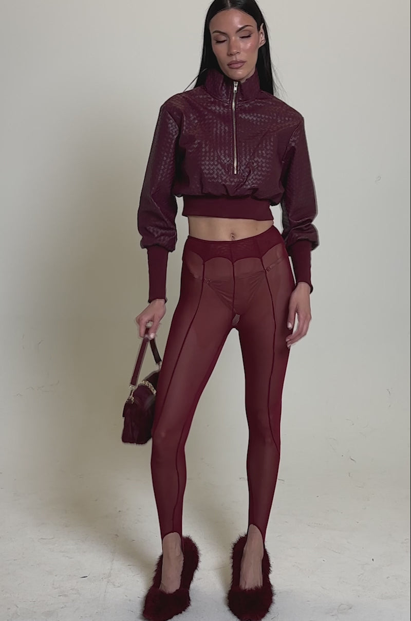 A video of a woman wearing shiny maroon outerwear, BALLET GIRL STIRRUP LEGGING IN BURGUNDY, maroon fuzzy slippers, and holding a small textured maroon handbag.