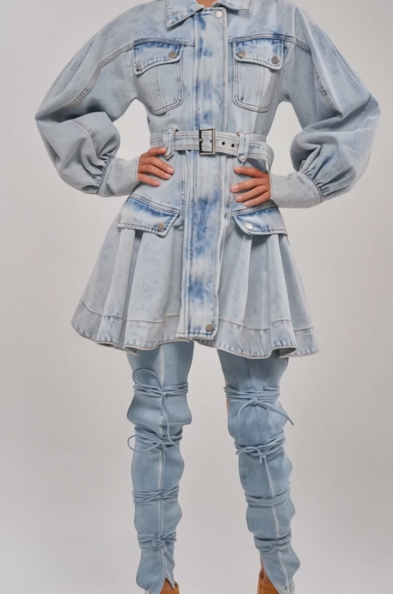 Video of woman modeling the SAY PRETTY PLEASE DENIM MINI DRESS, featuring a belted waist, oversized sleeves, and front pockets. She pairs it with large hoop earrings and pulled-back hair for a chic update on the classic denim dress look.